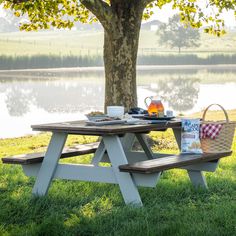 a picnic table set up in the grass near a tree with a basket on it