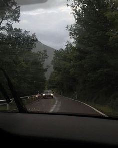 a car is driving down the road in front of some trees and mountains on a cloudy day