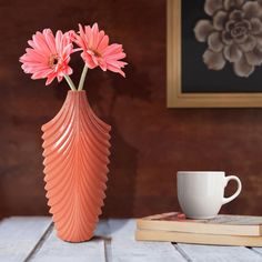 a pink vase with flowers in it next to a book and coffee cup on a table