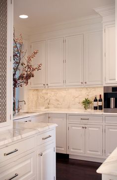 a kitchen with white cabinets and marble counter tops