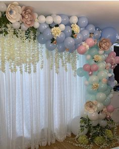 balloons and flowers are hanging on the wall in front of a window with sheer curtains