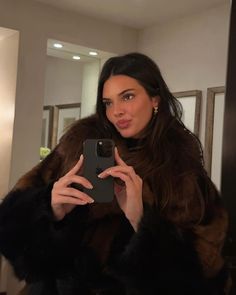 a woman taking a selfie in front of a mirror wearing a fur coat and holding a cell phone