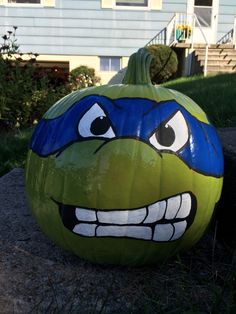 a painted pumpkin sitting on the ground in front of a house with an angry face