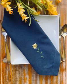 a blue napkin with embroidered daisies on it next to a fork and spoons