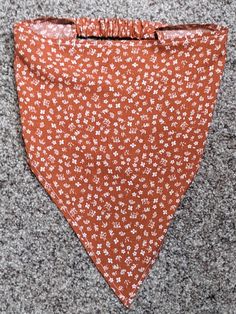 an orange bandana with white flowers on it is laying on the ground next to a gray carpet