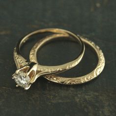 two gold wedding rings sitting on top of a black surface with a diamond in the middle