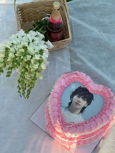 a pink heart shaped cake sitting on top of a table next to a basket filled with flowers