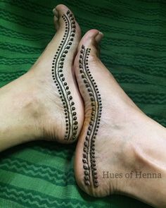 two feet with hendi tattoos on them laying on top of a green bed sheet