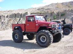 a red truck parked on top of a dirt road next to a mountain side covered in rocks