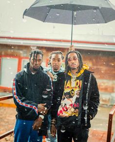 three men standing under an umbrella in the rain