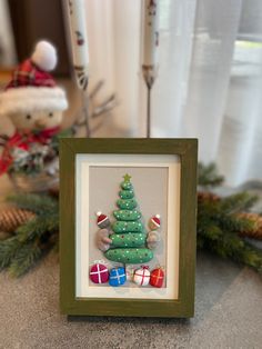 a small christmas tree is in a frame on the table next to some pine cones