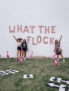 three girls standing in front of a sign that says what the flock? with pink flamingos