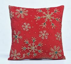 a red pillow with gold and green snowflakes on the front, sitting on a white surface