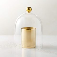 a gold cup under a glass clochet on a white countertop, with the lid partially closed