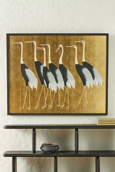 four birds are standing in front of a painting on the wall next to a shelf