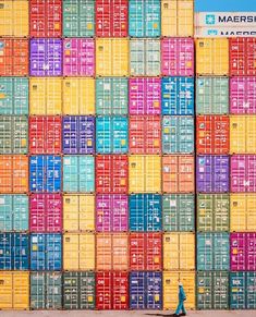 a man walking past a large stack of colorful shipping containers