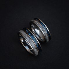 two wedding bands with blue and silver inlays are shown on a black surface