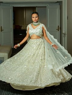 This ivory bridal lehenga set exudes elegance with intricate silver embroidery on a sleeveless blouse, a flowing lehenga skirt, and a sheer, delicately embroidered dupatta. Perfect for brides seeking a timeless and graceful look. Key Features: Color: Chiffron Off-White Components: Sleeveless blouse, full lehenga skirt, and sheer embroidered dupatta Design: Floral and geometric embroidery covering the entire set Dupatta: Sheer with embroidered edges for an elegant drape Occasion: Perfect for wedd Glamorous Wedding Sets With Resham Embroidery, Glamorous Georgette Anarkali Set For Wedding, Glamorous Wedding Traditional Wear With Resham Embroidery, Glamorous Gown With Saree Shape And Intricate Embroidery, Glamorous Gown With Intricate Embroidery In Saree Style, Elegant Off White Gown For Festive Occasions, Glamorous Lehenga With Intricate Embroidery In Georgette, Glamorous Lehenga In Georgette With Intricate Embroidery, Glamorous Georgette Lehenga With Intricate Embroidery