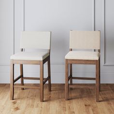 two white chairs sitting next to each other on top of a hard wood floor in front of a wall