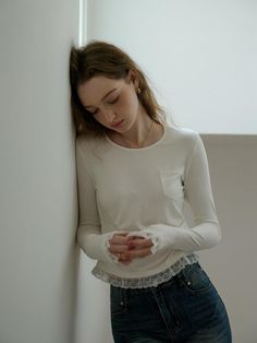 a woman leaning against a wall looking down at her cell phone while wearing a white shirt and jeans