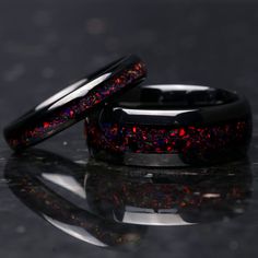 two black wedding bands with red and blue glitter inlays, on a reflective surface