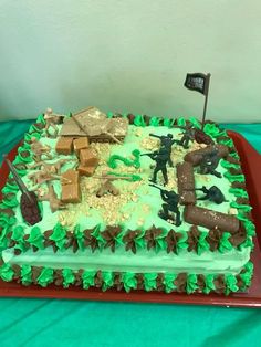 a cake with green frosting and soldiers on it, sitting on a tablecloth