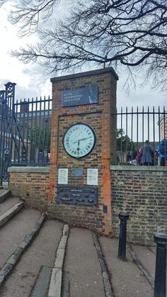 a brick clock tower sitting on the side of a road next to a metal fence