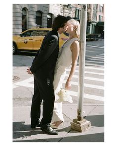 a man and woman kissing in front of a street sign on the side of the road