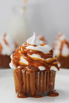 some cupcakes with caramel and whipped cream on top are sitting on a white plate