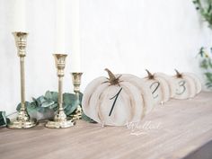 some white pumpkins sitting on top of a wooden table next to candles and greenery