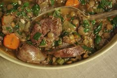 a bowl filled with meat, beans and vegetables next to a spoon on top of a table