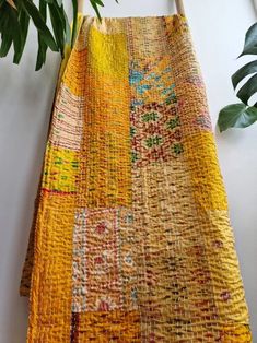 a yellow and multicolored rug hanging on a wall next to a potted plant