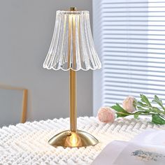 a table with a lamp on top of it and flowers in front of the window