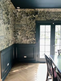 a dining room with wallpaper and chairs in front of a door that leads to another room