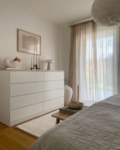 a bedroom with white furniture and curtains on the windowsill, along with a large bed