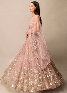 Step into the spotlight with this Lavender Pink Gold Sequinned Lehenga Set. The tulle fabric beautifully showcases hand-embroidered mirror flower motifs that add a touch of sparkle. Complete with a filly embellished blouse and a delicate tulle dupatta featuring a statement scalloped border, this set is the epitome of elegance and glamour. Composition: Lehenga, Dupatta and Blouse - Soft Tulle All products can be customised for sleeves, length of blouse and neck design Delivery : 4-6 weeks as the product is hand crafted. Check Size Guide or choose MySize for free customisation (All Sizes above XL can be made at 15% additional cost) For more information and sizes please contact fabiliciousfashion@gmail.com or visit our Copenhagen studio. Elegant Embroidered Net Lehenga, Pink Embroidered Net Lehenga, Embroidered Fabric With Sequins For Wedding, Embellished Net Dress For Diwali, Pink Net Lehenga With Resham Embroidery, Designer Sequined Organza Gown, Fitted Bollywood Net Gown, Embroidered Net Dress For Reception, Floor-length Sequin Fabric With Mirror Work For Reception