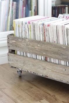 a wooden crate filled with magazines on top of a hard wood floor next to a bookshelf