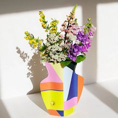 a vase filled with lots of colorful flowers on top of a white table next to a window