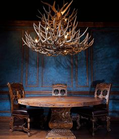 a dining room table and chairs with antlers on the chandelier above it