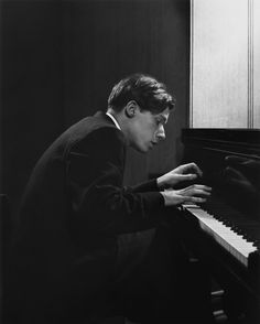 a man sitting at a piano in front of a black and white photo with his hands on the keyboard