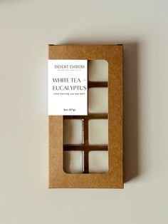 four white tea eucalyptus candles in a cardboard box on a white surface with a brown label