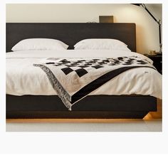 a bed with a black headboard and white sheets on top of it, next to a night stand