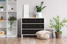 a black and white dresser sitting in a living room next to a potted plant