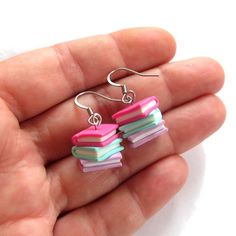 a hand holding a pair of colorful book earrings