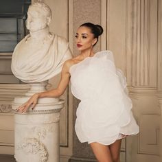 a woman in a white dress standing next to a statue