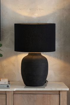 a large black vase sitting on top of a table next to a lamp with a black shade