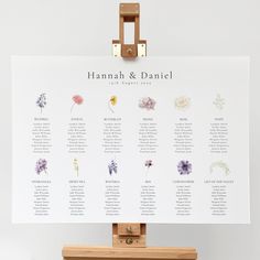 a wooden easer holding a seating chart with flowers on it and the names of each table