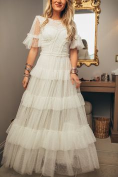 a woman standing in front of a mirror wearing a white dress with tiered layers