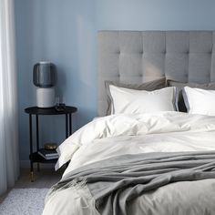 a bed with white sheets and pillows next to a night stand in a room that has blue walls