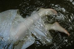 a woman is floating in the water wearing a white dress and holding onto her leg